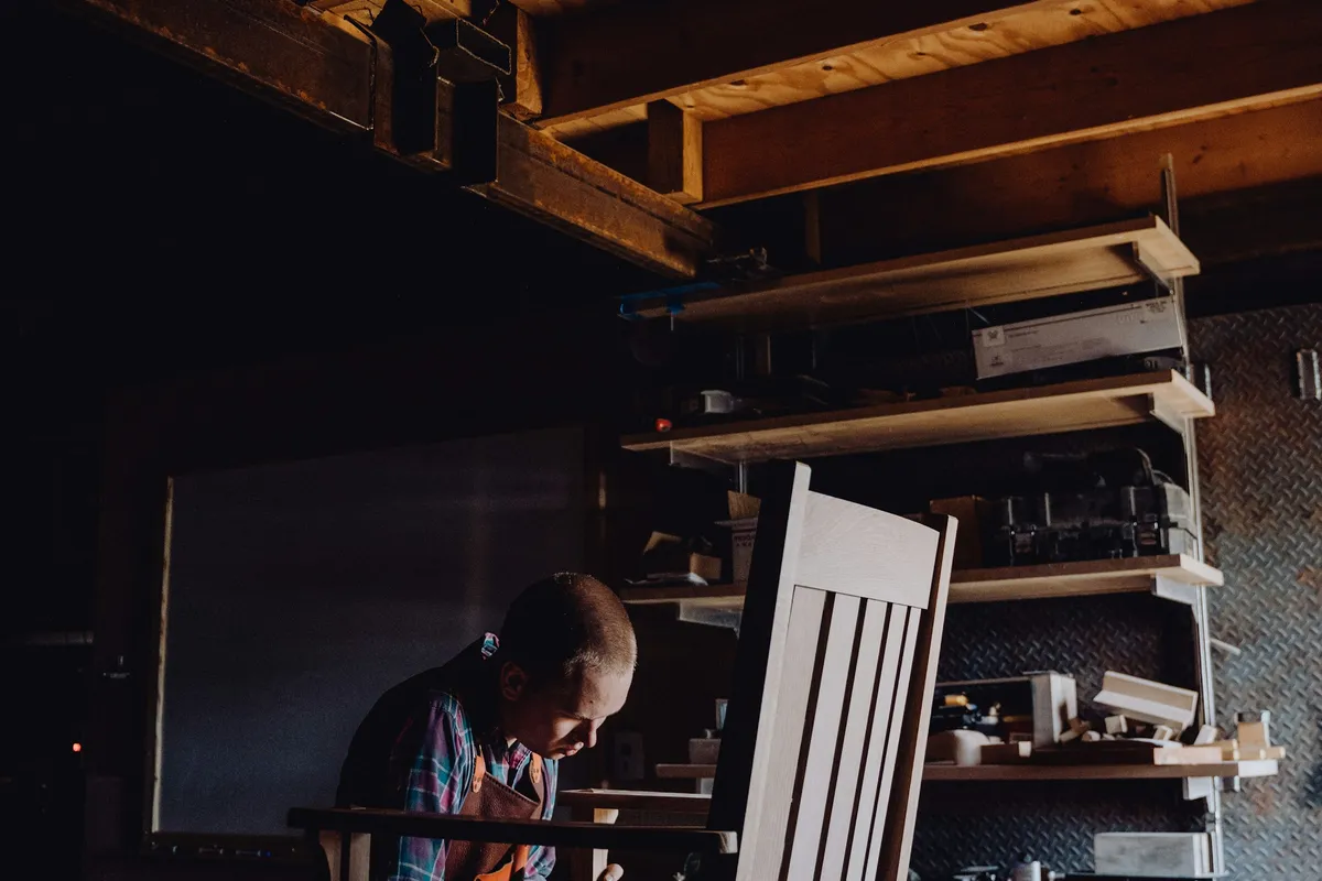 A carpenter shaping the joints of a wooden chair frame in his workshop