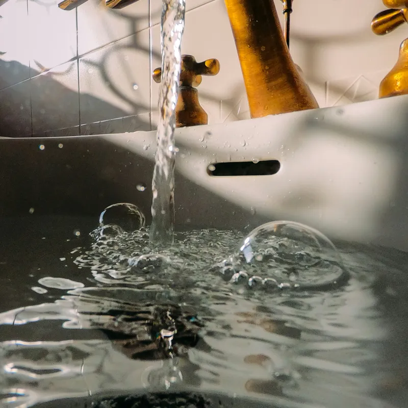 A brass bathroom tap running clear into a filled basin