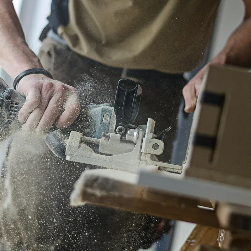 A tradesman cutting a joint into a piece of lumber, sawdust in the air